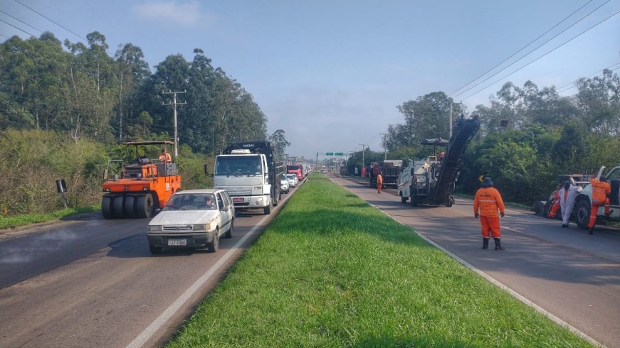 A foto mostra a rodovia dividida por um canteiro central gramado. em ambos os lados, trabalhadores e máquinas se misturam para a realização de obras. 